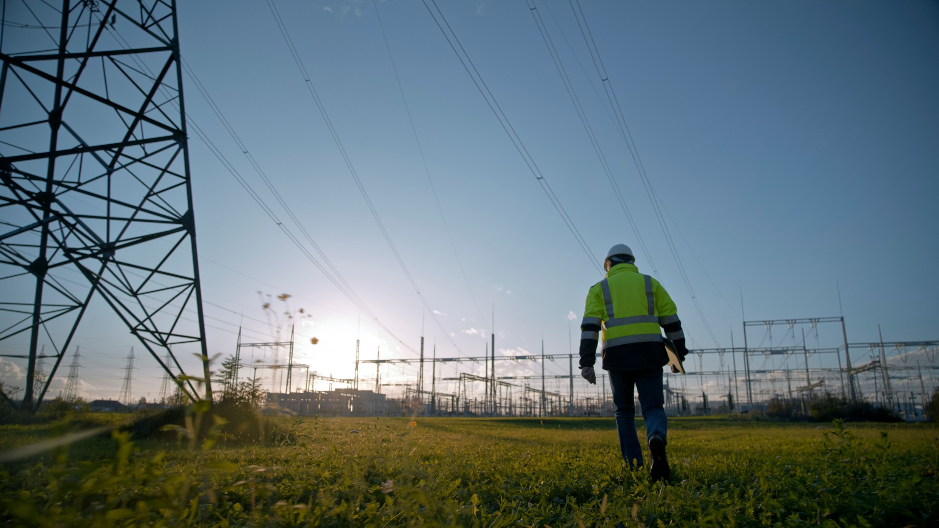 Rear View Of Electrical Engineer Holding Laptop While Walking At Power Station During Sunset